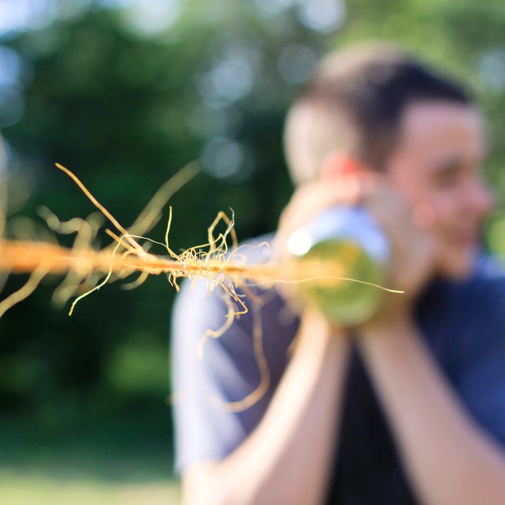 Junger Mann spielt im Garten mit Dose und Seil das Telefonieren nach